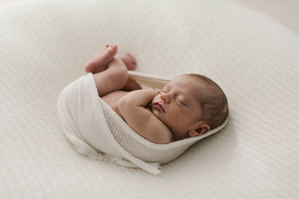 newborn baby laying on a white blanket and ivory wrap in a simple and neutral set up. Photo by Laurie Baker 
