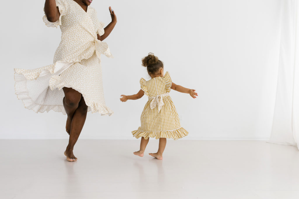 a woman in a yellow floral dress dancing with her daughter in a butterscotch colored dress