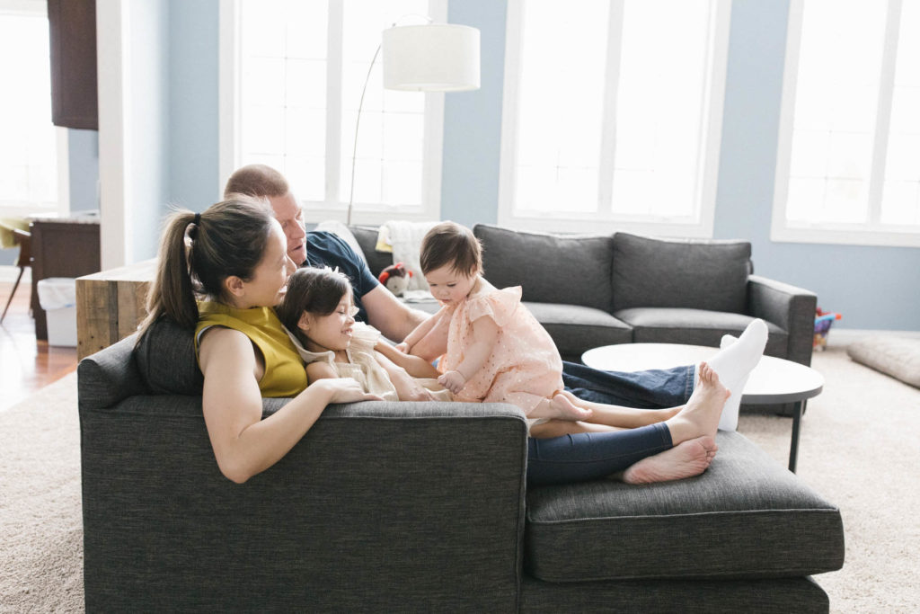 Family of four sit on the couch with beautiful natural light windows 
