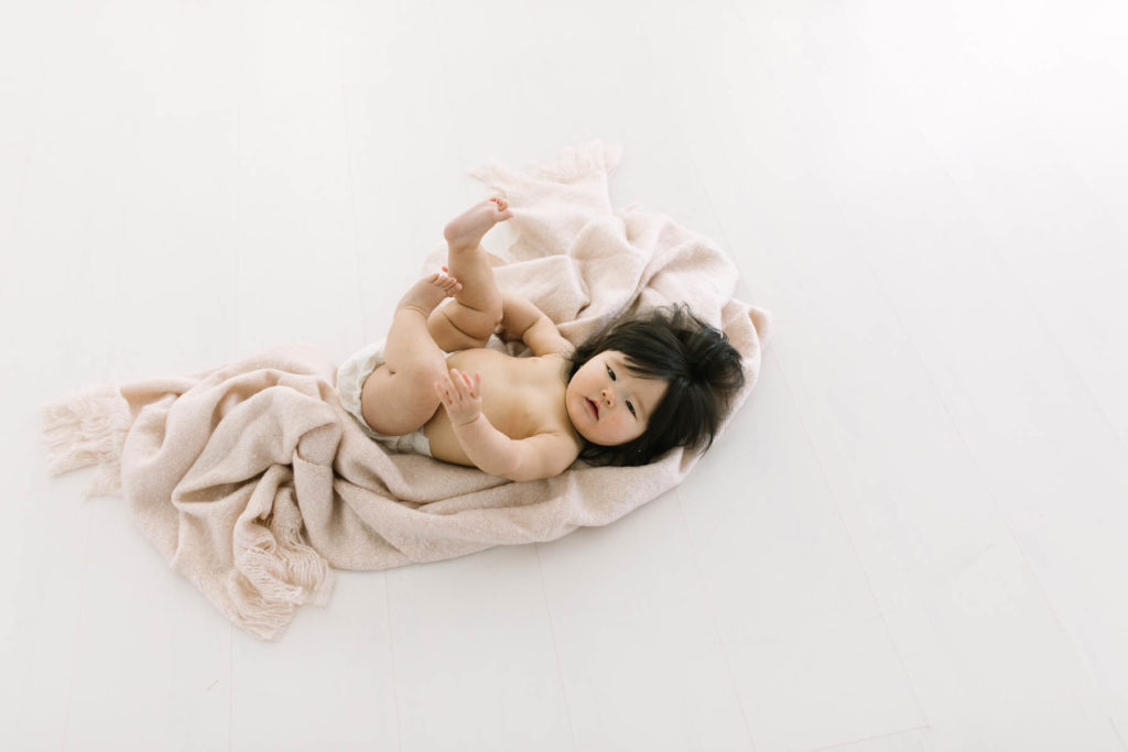 baby girl lays on a blush colored blanket in a white studio in Naperville IL 
