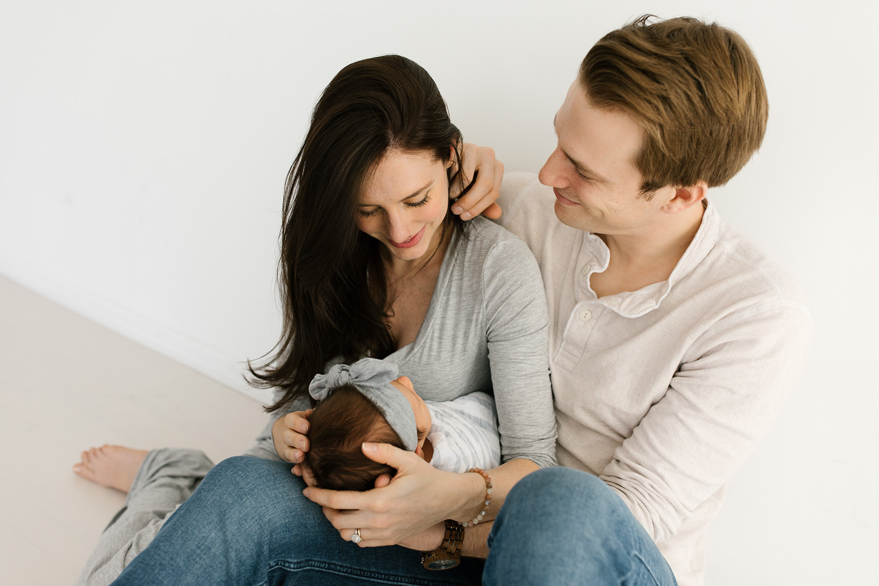 husband gently moving hair from his wife's neck and holding newborn baby