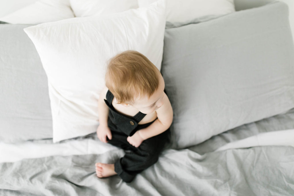 Baby boy sits on a bed during first birthday photo shoot 