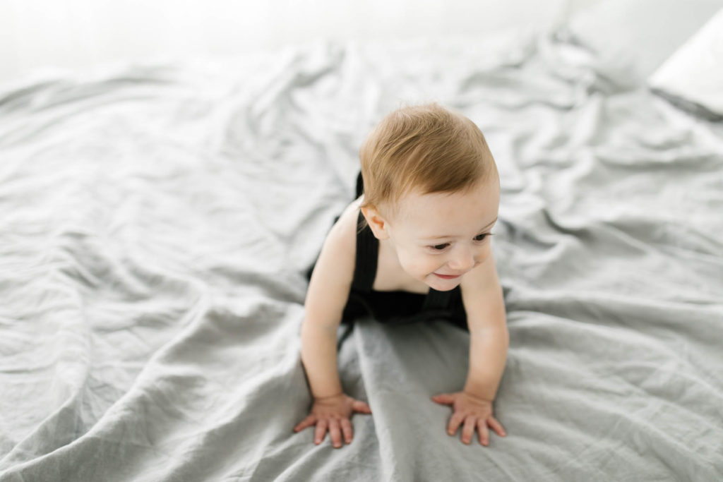 baby boy crawling around on a bed during a first birthday photo session 