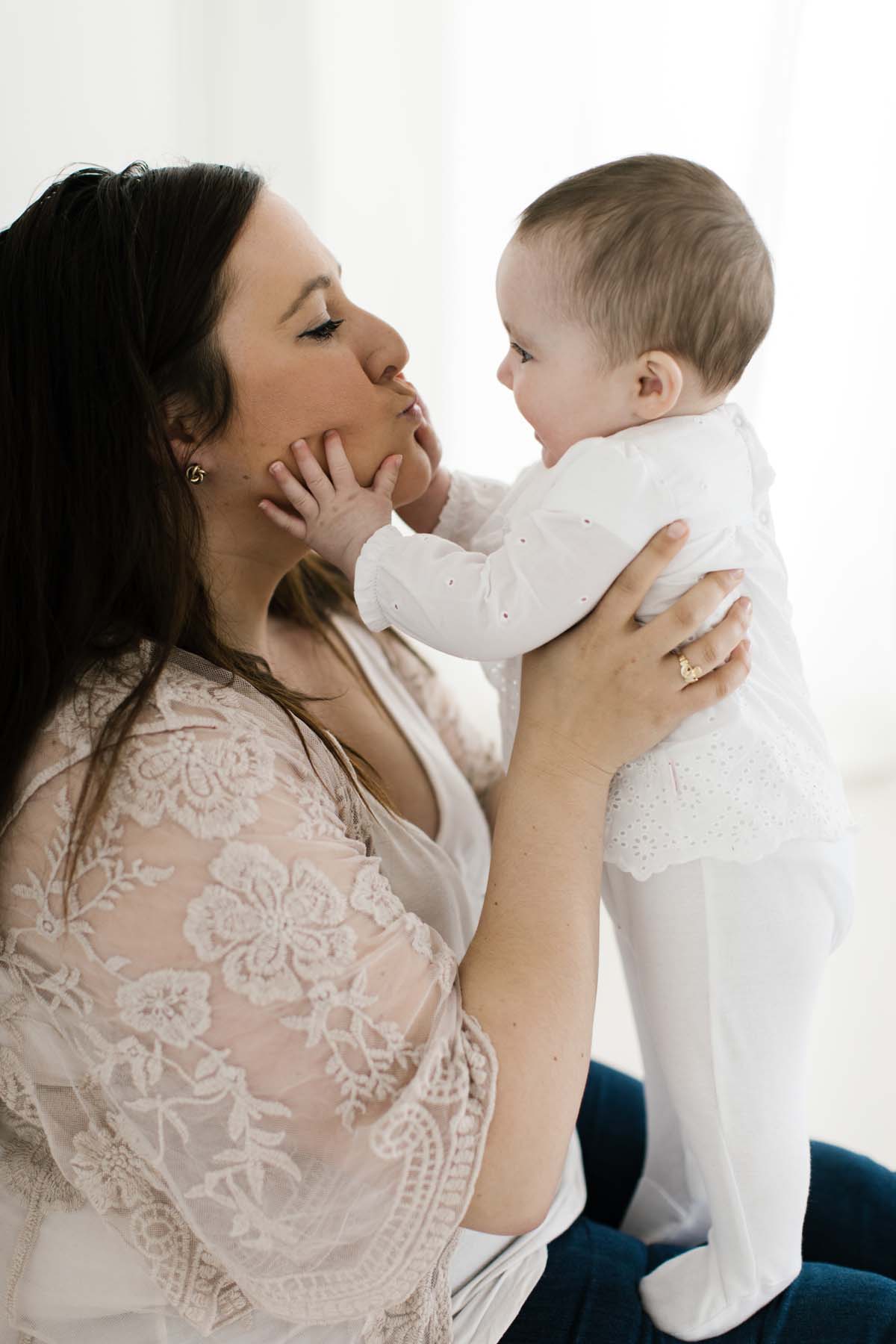 mom kisses baby girl in white layette 