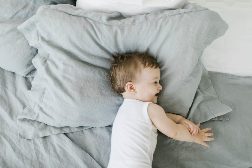 giggling baby boy on bed with gray linen bedding 