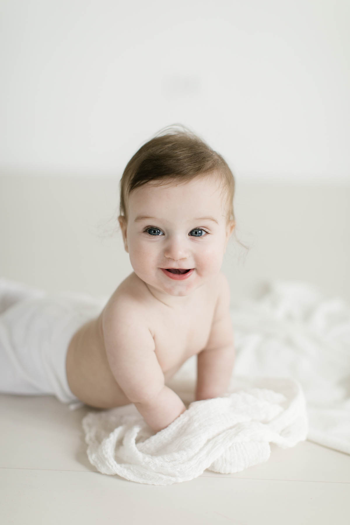 baby boy smiles and looks at his mom during his six month milestone session 