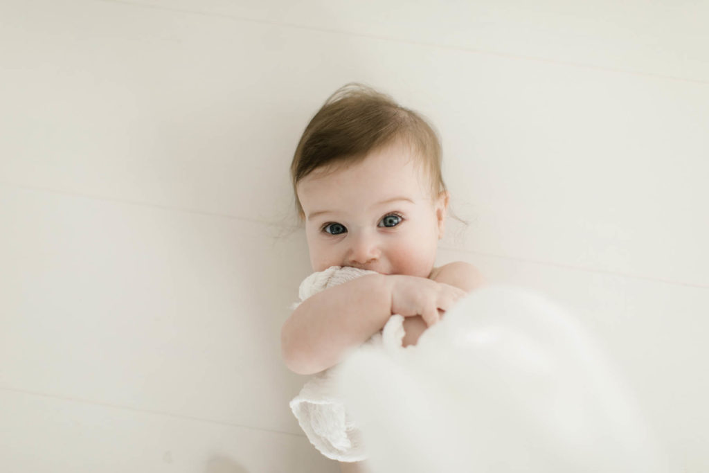 baby boy plays with a white curtain at a six month milestone session