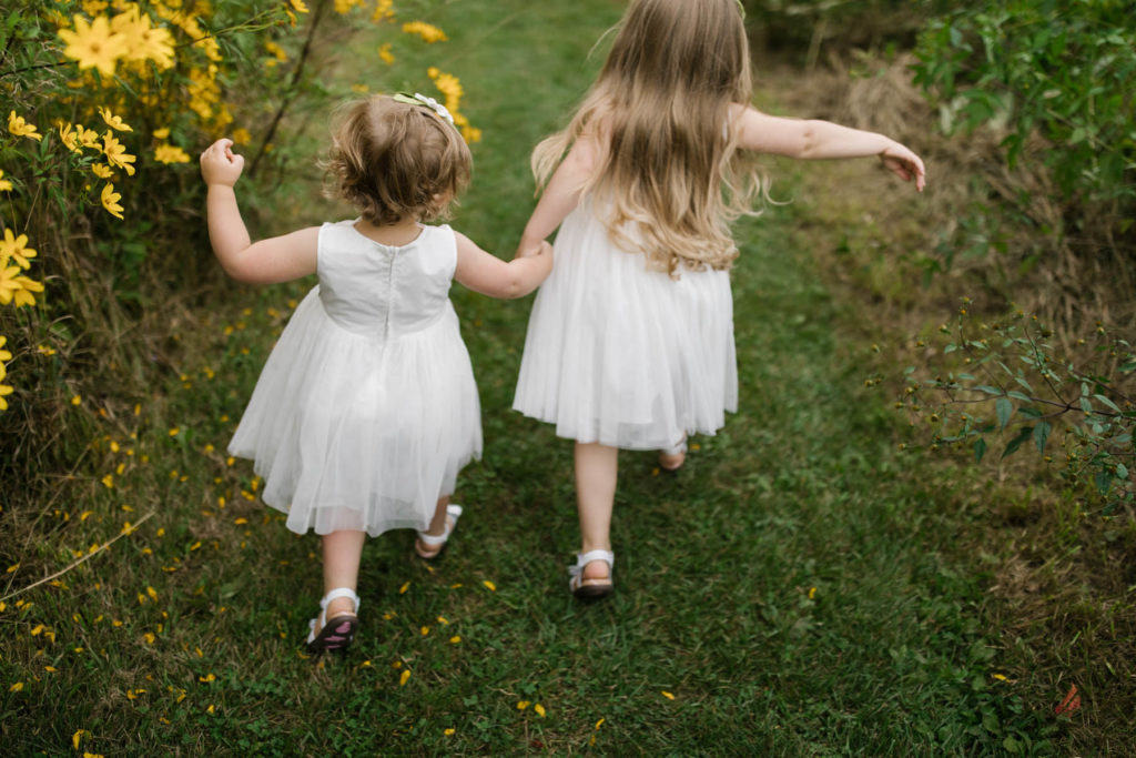 little girls holding hands and running in white dresses 