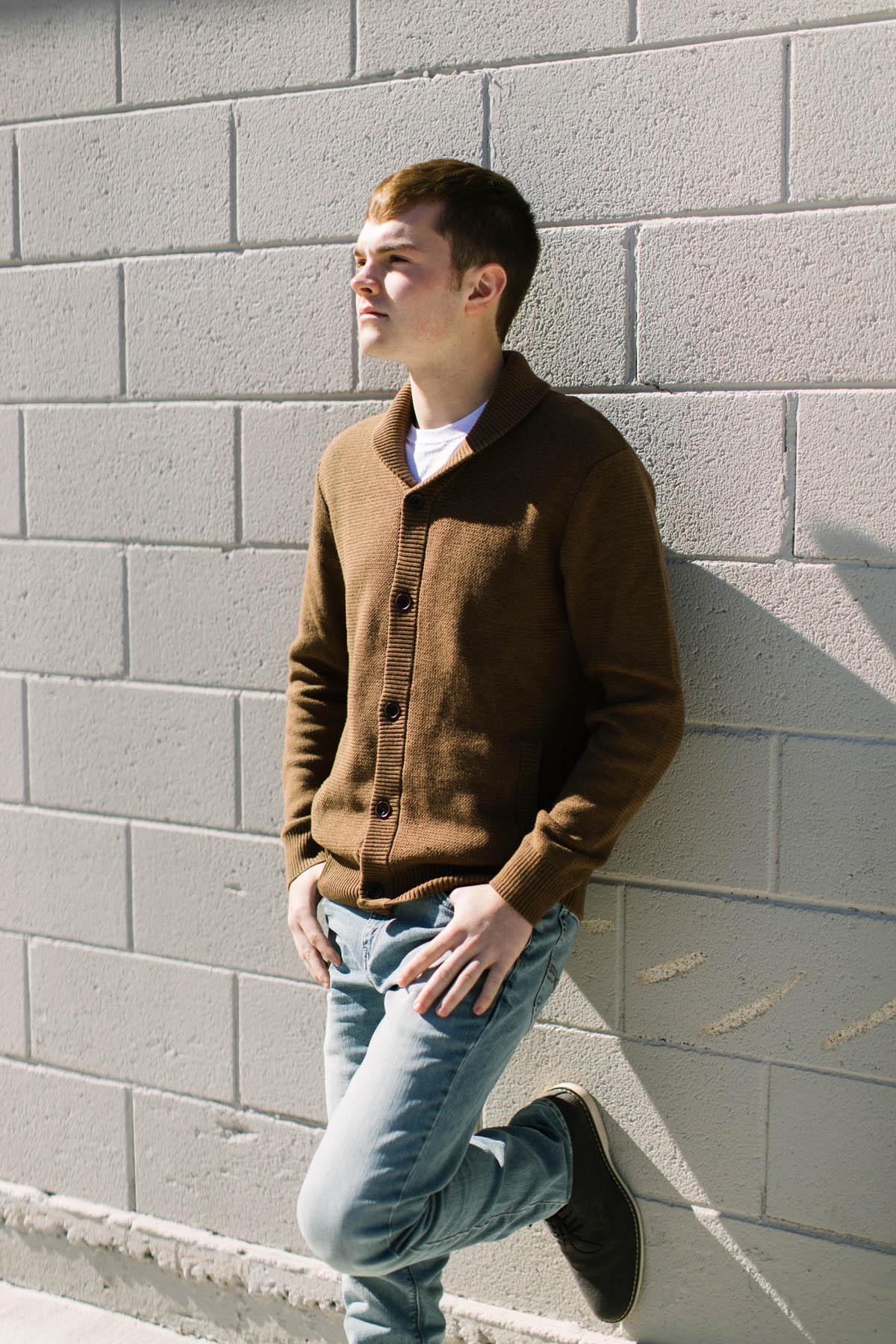 high school senior photography session, boy leans up against the wall in direct sunlight 