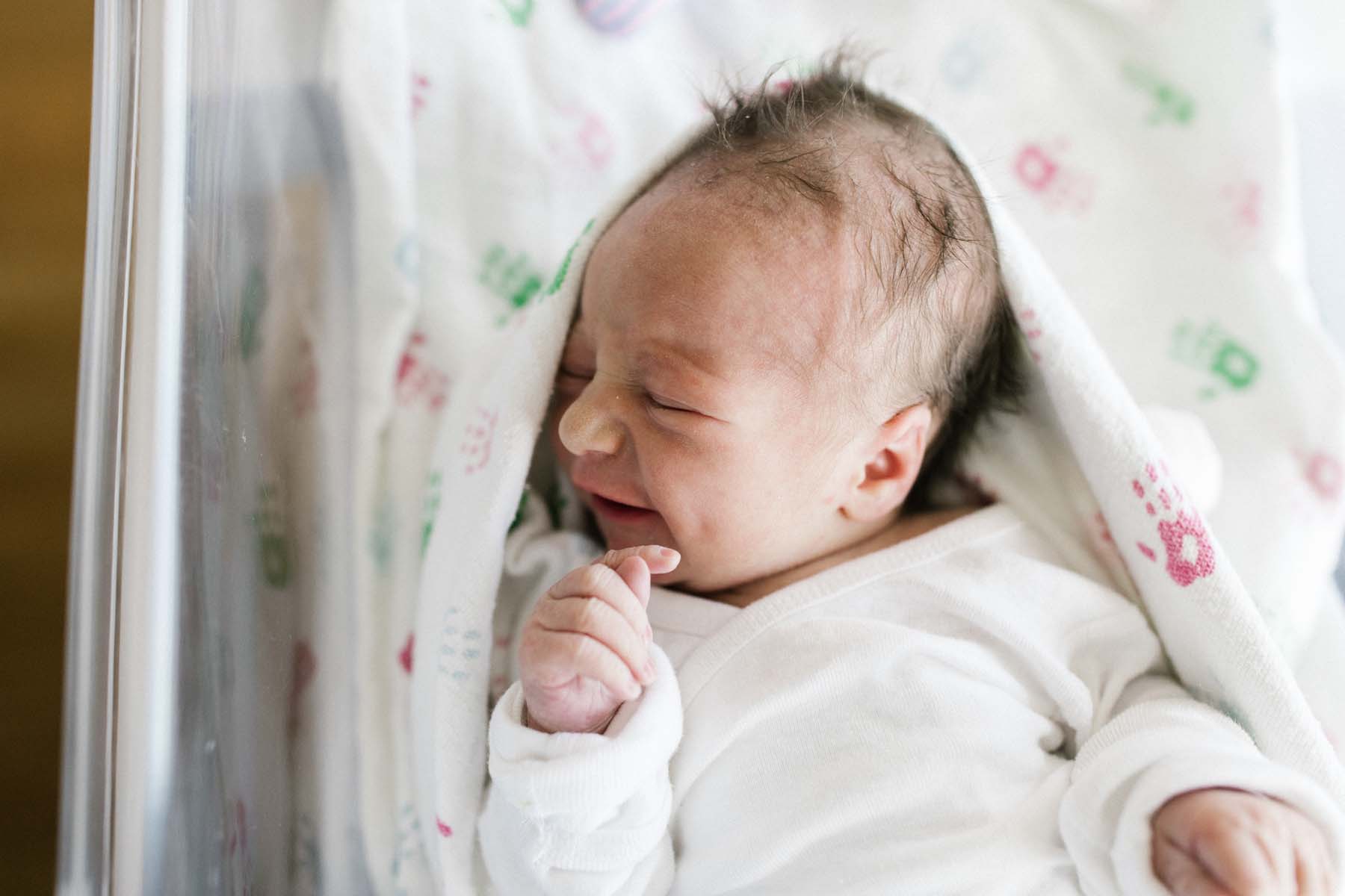 newborn baby smiling with dimple in hospital bassinet