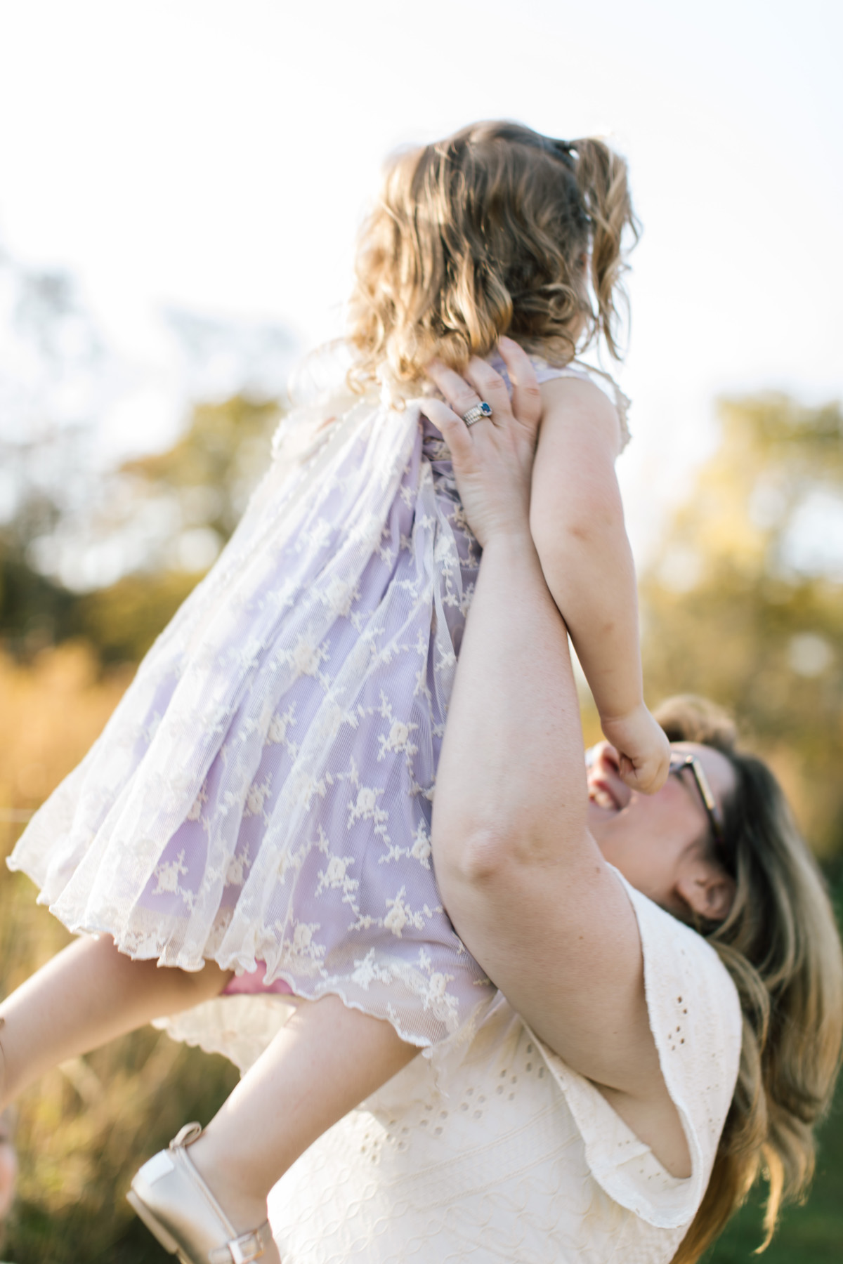 mom lifting her daughter into the air wearing a lilac dress with light all around her