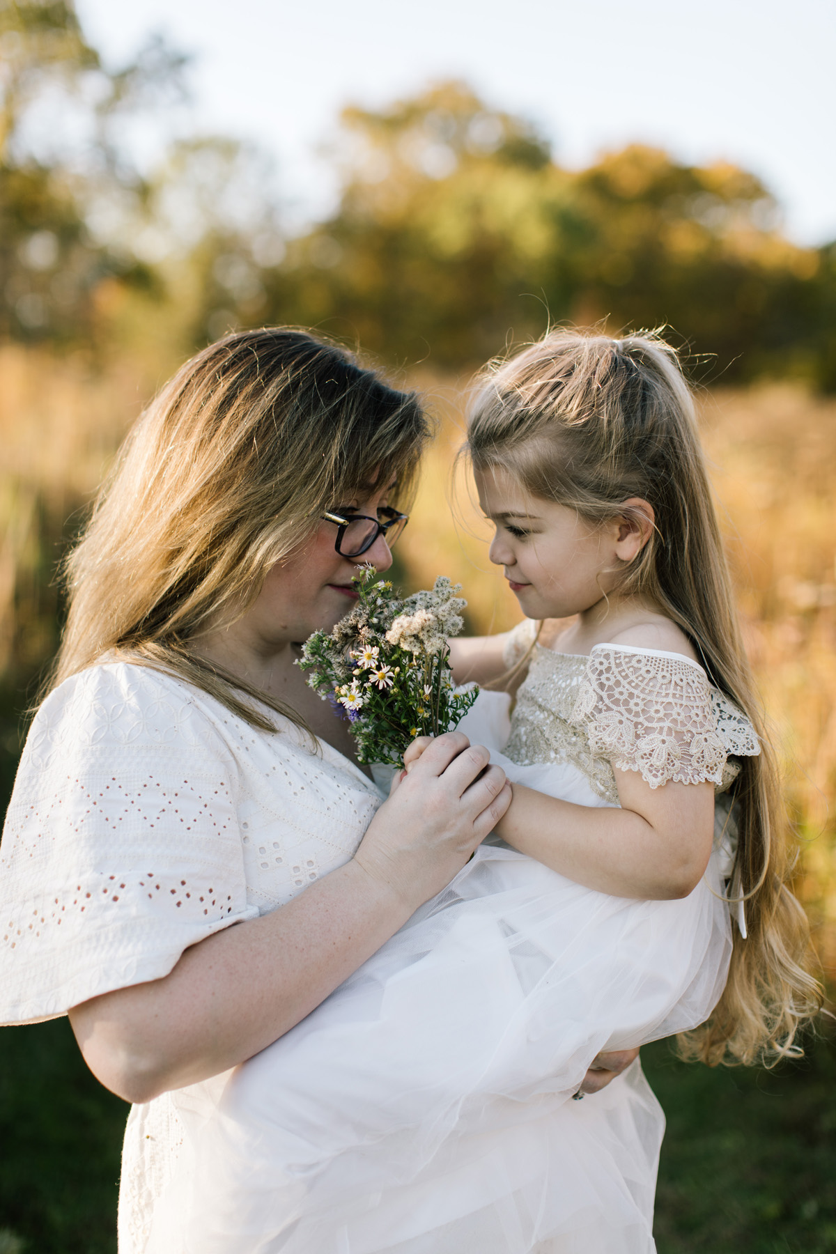 mom and daughter smelling wildflowers during a session with light all around them