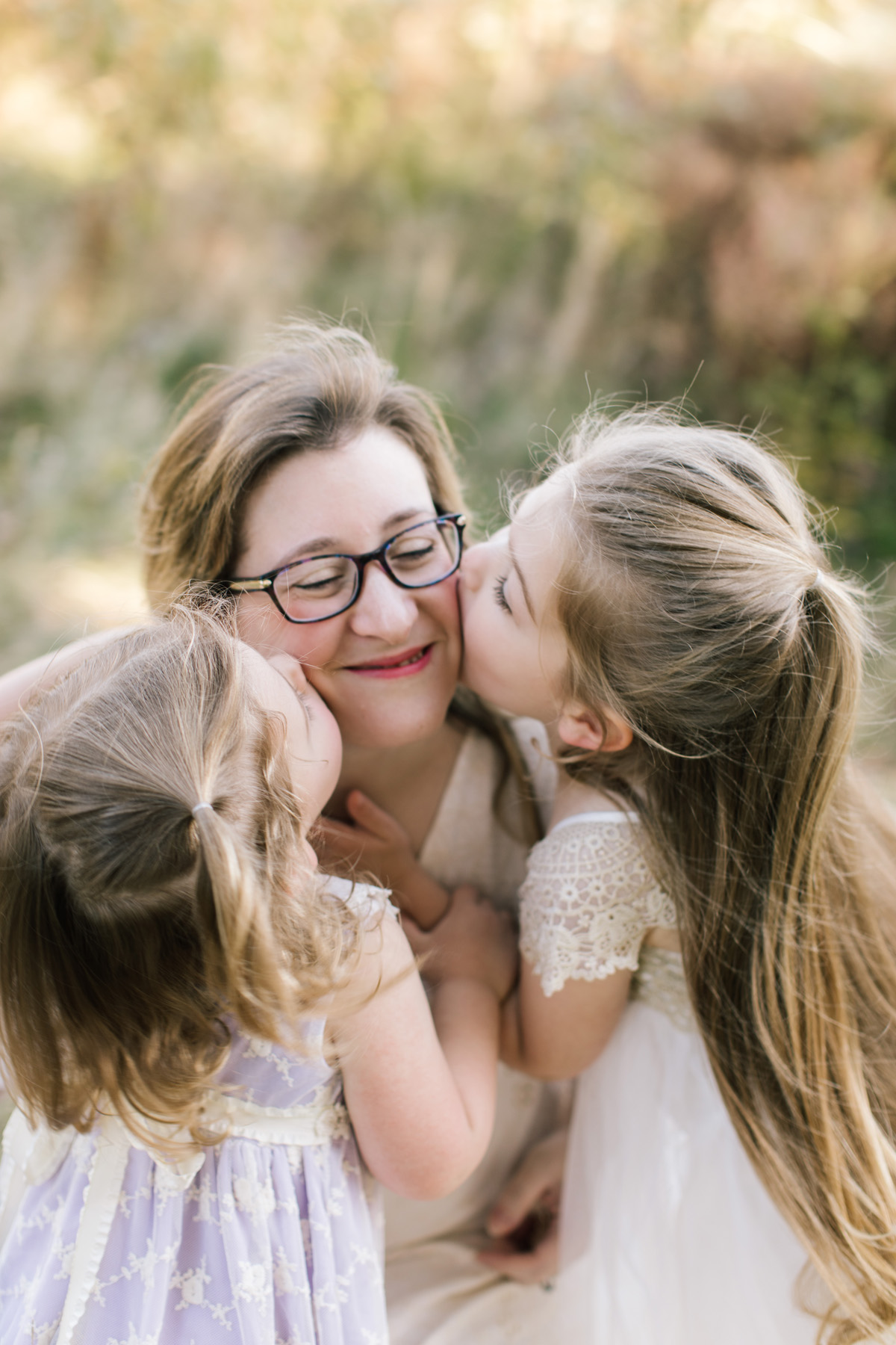 two little girls kissing their mom on the cheek 
