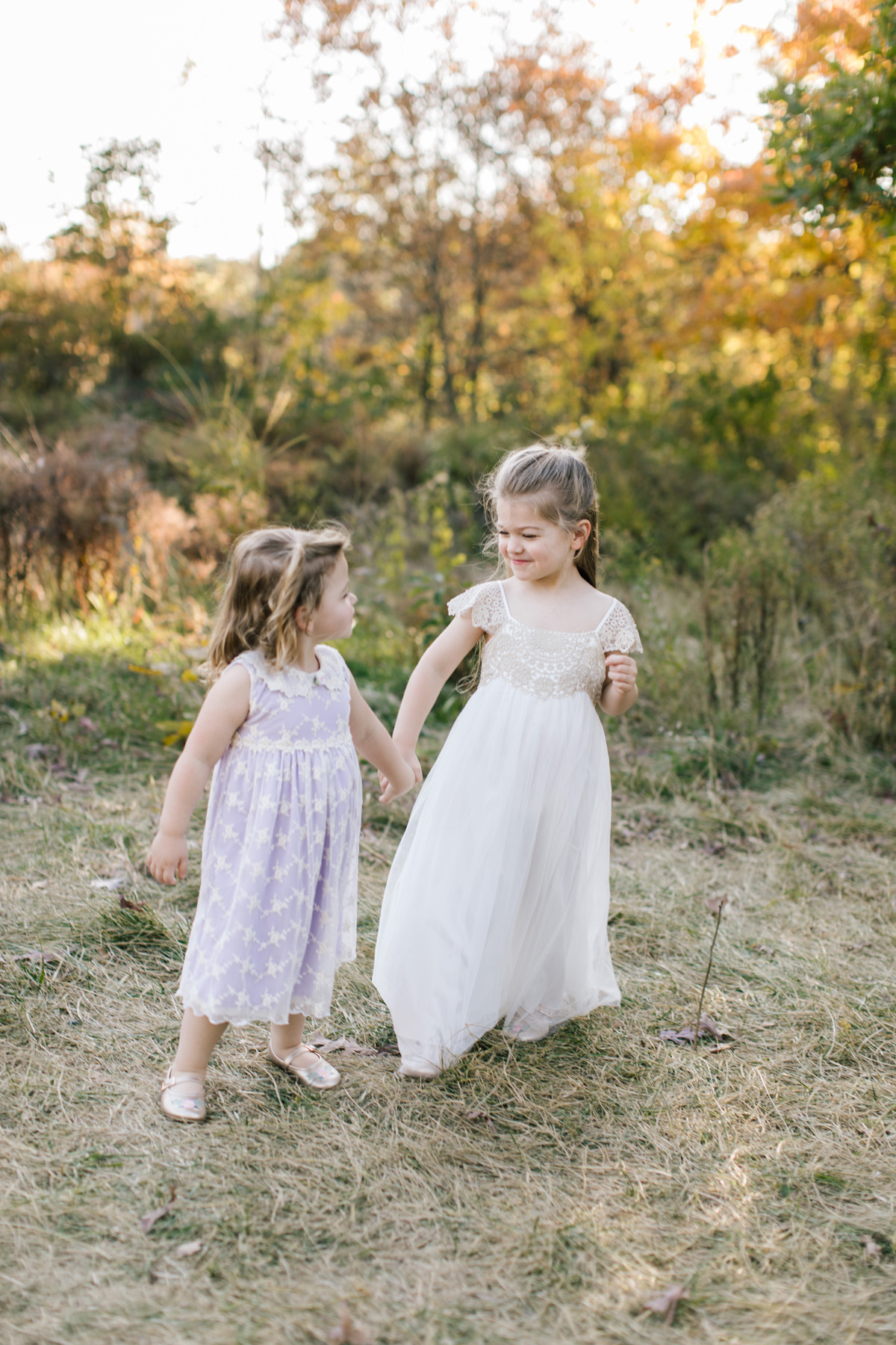 two sweet girls holding hands in a forest preserve smelling flowers 