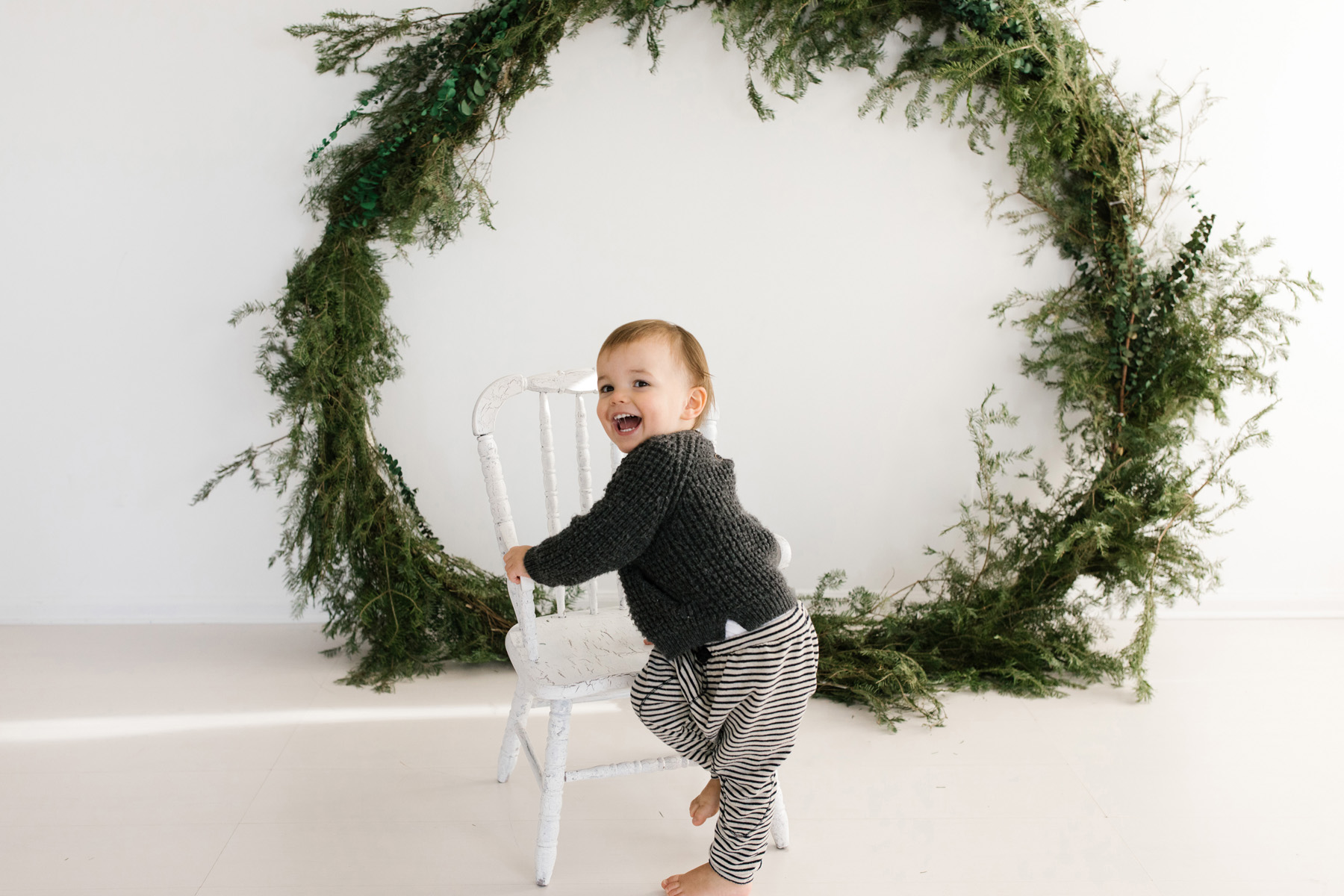 child sitting on white stool with wreath in the background