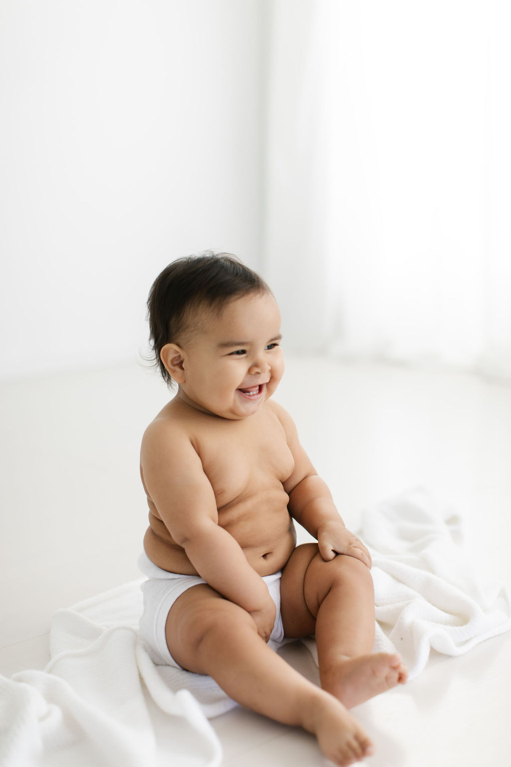 baby smiling sitting on a white blanket 