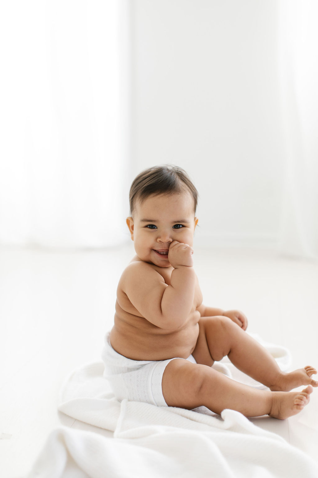 photograph of baby sitting in a white simple studio during baby's first birthday sessions