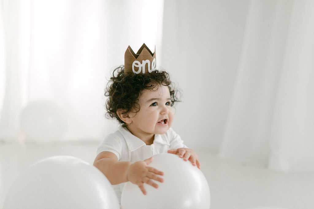 baby holding white balloons during his baby's first birthday photos
