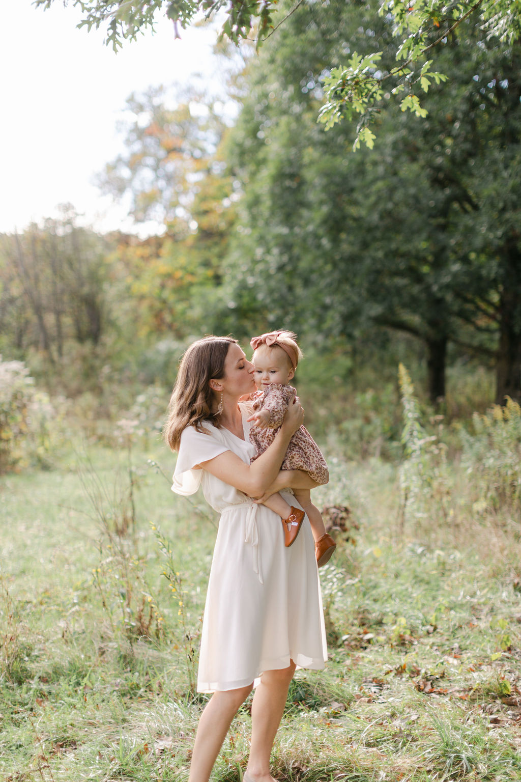 mom kissing baby girl on the cheek outdoors at a photo session